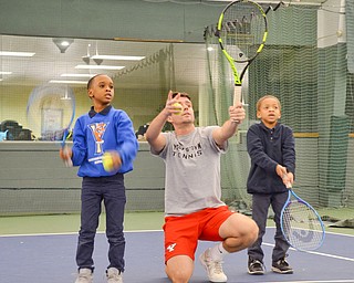 Pol Virgili Blanco, YSU sophomore international business major from Spain, coaches Ja'Viere Woods, left; first grade, and Sergio Shaw, right; kindergarten, both students from Youngstown Community School, on how to swing a tennis racket at the Boardman Tennis Center on March 23, 2018.  

Photo by Scott Williams - The Vindicator 