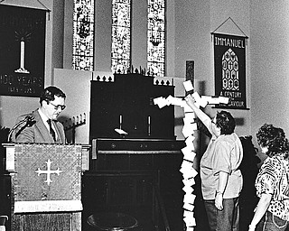 REPENTANCE ON GOOD FRIDAY: The Rev. James Juergenson, left, pastor of Immanuel Lutheran Church, Guadalupe Avenue at Redondo Road, reads meditation as Gloria Jacobs, center, pins symbolic "sins" on the cross,  Luanne Shick, right, awaits her turn to pin away "sins."  The cross and the "pinning of sins" will be used during services on Good Friday to dramatize the meaning of Christ's crucifixion.  

Photo taken April 8, 1987.  

Photo by Robert DeMay - The Vindicator