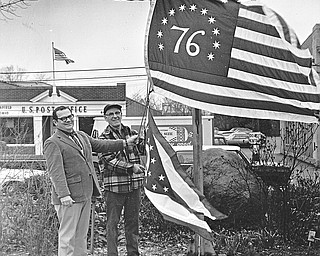 BICENTENNIAL FLAG - Canfield City officials Friday hoisted two new flags, which will be flown over the Village Green day and night for the duration of the bicentennial celebration.  Left is City Manager Chris Paparodis with Orville Paugh, superintendent of parks and streets.  Regular flags were lowered and the Bennington flag - which has 13 stripes of red and white on a field of blue, 13 stars and numeral "76," was raised.  Below the American flag is a newly purchased Ohio State Flag.

Photo published April 19, 1975.