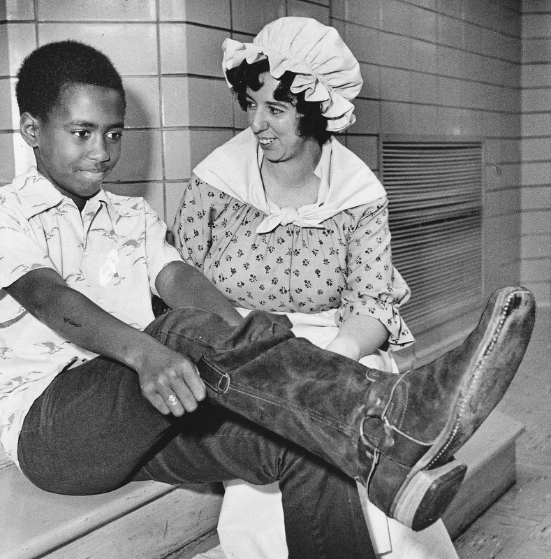 STYLES FROM THE PAST - Darren Boatwright finds it takes some pulling to get into an old-fashioned boot.  Mrs Paul Hunter, Junior League member, wears a dress which might have been in style when such boots were the fashion.

Photo published Saturday, November 1, 1975.

Photo by Paul R. Schell