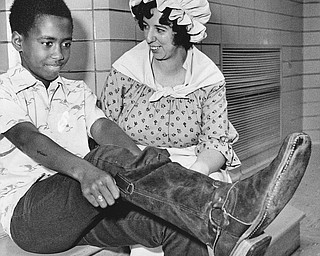 STYLES FROM THE PAST - Darren Boatwright finds it takes some pulling to get into an old-fashioned boot.  Mrs Paul Hunter, Junior League member, wears a dress which might have been in style when such boots were the fashion.

Photo published Saturday, November 1, 1975.

Photo by Paul R. Schell