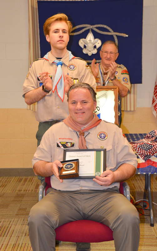 John Russell, seated, is applauded by his son Colin, left, and Bill Moss, district training chairman, after receiving the District Award of Merit at the Whispering Pines Boy Scouts Recognition Dinner at St. James Episcopal Church in Boardman on Sunday, April 15, 2018. The award is available to registered Scouters who render service of an outstanding nature at the district level.

Photo by Scott Williams - The Vindicator