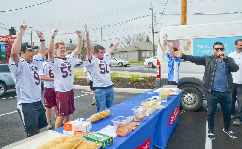 Members of the Boardman High School Lacrosse team, from left to right, #9 - Devin Whitaker, #55 - Clayton Wehr, and #50 - Cody Geary, participated in a "Sub Off" challenge, racing each other to make the most subs in three minutes at the grand-opening ceremony of the new GetGo gas station/cafe/market at 133 Boardman-Poland Road in Boardman on Thursday May 3, 2018.  On the right in black is celebrity chef Adam Richman. 

Photo by Scott Williams - The Vindicator