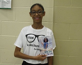 Neighbors | Zack Shively.Reagan Nevels, seventh-grade student at Austintown Middle School, gave a presentation on the book she wrote, "Vision Collision," in the school's cafetorium on May 22. Pictured, Nevels heldsher book and wores her shirt.