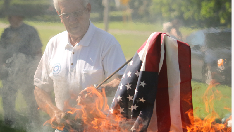 Bob Kirchner of American Legion Post 301 holds a flag in the flames during Austintown’s flag-burning ceremony Thursday in the Veterans’ Memorial Park.