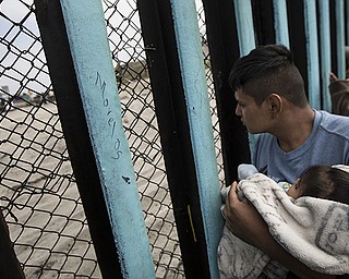 A man a child looks through the border wall toward a group of people gathered on the U.S. side, as he stands on the beach where the border wall ends in the ocean, in Tijuana, Mexico.