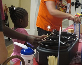 Neighbors | Jessica Harker .Alexis Newell prepared to dunk her marshmallow into melted chocolate during the June 22 camp out at the Poland library.
