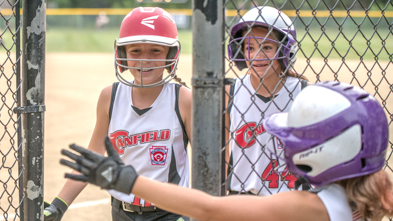 Canfield's Sam Economous, left, and Riley Billak, center, are all smiles returning to the dugout after scoring and are congratulated by teammate Brooke Opalick during 10-U state tournament action in Tallmadge on Monday. Canfield won 18-4 against Austintown.