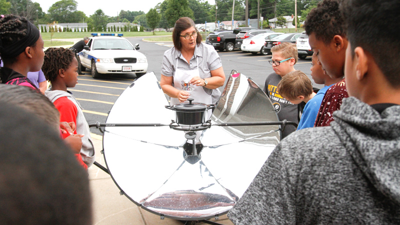 Jennifer Gasser of Hubbard, one of the Solar Sisters, explains how a parabolic solar cooker works to Paul C. Bunn Elementary School summer school students in Youngstown.