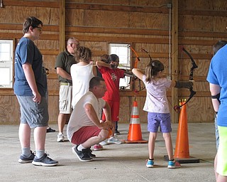 Neighbors | Jessica Harker .4H volunteer instructor Steve Adams knelt behind students as they prepared to shoot at designated targets at the annual archery camp at MetroParks Farms.