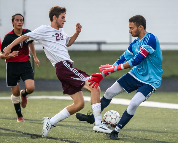 DIANNA OATRIDGE | THE VINDICATOR Boardman's Tommy Fryda (20) shoots between the legs of Canfield goalkeeper Jad Jadallah as Canfield's Antonio Santiago looks on during their game at Bob Dove Field in Canfield on Thursday. The Spartans won 4-1.