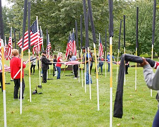 Volunteers help take down, roll, and bag the flags after the closing ceremonies for the traveling memorial on Sunday. EMILY MATTHEWS | THE VINDICATOR