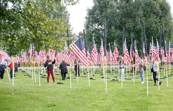 Volunteers help take down, roll, and bag the flags after the closing ceremonies for the traveling memorial on Sunday. EMILY MATTHEWS | THE VINDICATOR