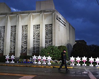 In this Oct. 28, 2018, file photo a Pittsburgh police officer walks past the Tree of Life Synagogue and a memorial of flowers and stars in Pittsburgh in remembrance of those killed and injured when a shooter opened fire during services Saturday at the synagogue. The perpetrators of mass shootings often provide a treasure trove of insight into their violent tendencies on social media. But the information is not always seen by law enforcement until after the violence is carried out.