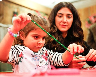 Aria Ries, 5, of Niles, puts beads onto a pipe cleaner to make a Christmas ornament with her mom Gina Ries at the Memories of Christmas Past exhibition at The Arms Family Museum on Saturday. EMILY MATTHEWS | THE VINDICATOR