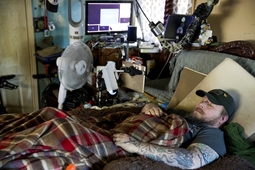 In this Friday, Nov. 16, 2018 photo, Jim Taft watches The History Channel from the confines of his bed at his home in West Columbia, S.C. Taft has experienced debilitating health issues after a neurosurgeon implanted Boston Scientific's Precision spinal cord stimulator in his back in 2014. 