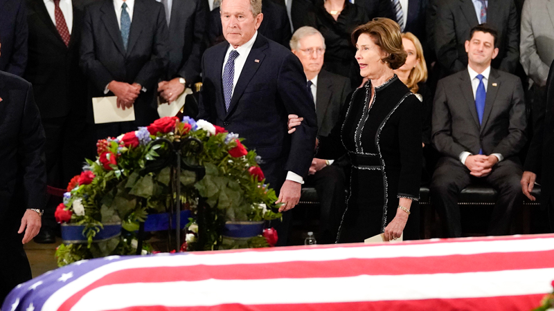 Former President George W. Bush and his wife, former first lady Laura Bush, pass by the flag-draped coffin of his father, former President George H.W. Bush, in the Capitol Rotunda in Washington on Monday afternoon.  