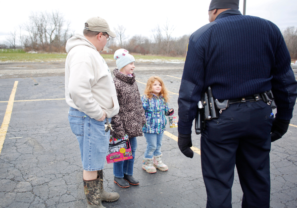 From left, Chris Philips and his daughters Kera Philips, 11, and Fiona Philips, 4, all of Austintown, hold toys to give to Officer Melvin Johnson, right, at Youngstown Police Department's fourth annual fill a cruiser campaign in the St. Christine Church parking lot on Saturday afternoon. EMILY MATTHEWS | THE VINDICATOR
