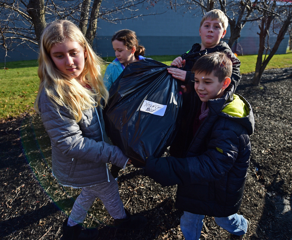 COLUMBIANA, OHIO - DECEMBER 13, 2018: (LtoR) Lily Robinson, Melina Carrabbia, Brody Sanders, Michael Gerthung, all 5th graders at Springfield Intermediate School, carry a bag of gifts from the back of a school bus, Thursday morning in Columbiana. DAVID DERMER | THE VINDICATOR