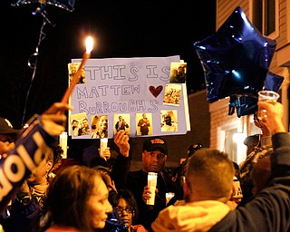 People hold up a poster for Matthew Burroughs as well as candles and balloons before releasing the balloons at the end of a vigil for Burroughs outside of his Royal Mall Apartment on Saturday night. EMILY MATTHEWS | THE VINDICATOR