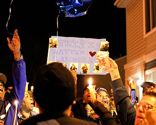 People hold up a poster and candles for Matthew Burroughs as balloons are released at the end of a vigil for Burroughs outside of his Royal Mall Apartment on Saturday night. EMILY MATTHEWS | THE VINDICATOR