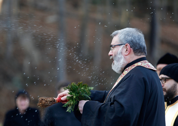 Father Tom Constantine blesses attendees with holy water during the Blessing of the Waters Service at Lake Glacier in Mill Creek Park on Sunday afternoon. EMILY MATTHEWS | THE VINDICATOR