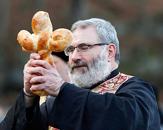 Father Tom Constantine holds up a cross made of bread before tossing it into Lake Glacier during the Blessing of the Waters Service at Lake Glacier in Mill Creek Park on Sunday afternoon. EMILY MATTHEWS | THE VINDICATOR