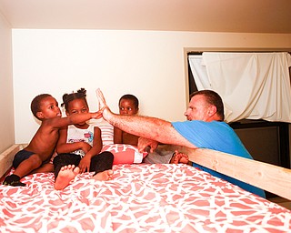 Dane "Mickey" Carder, of Canfield, high-fives, Xyayion Dotson, 3, while Miracle Morgan, 5, and Zion Johnson, 4,  sit in the top bunk of their new bunk bed from Sleep in Heavenly Peace in the kids' home in Campbell on Saturday night. Sleep in Heavenly Peace, the group that Carder is the Youngstown chapter president of, measured, cut, and stained the pieces of the bed during the day and then brought the pieces to the home and built the bunk bed there at night. Prior to receiving the bunk bed, the three children were sharing one mattress.