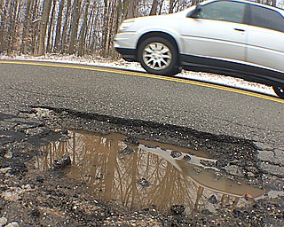 A car speeds by a spot on Shields Road in Canfield where the edge of the road has crumbled following the first major snow and thaw of the winter. 