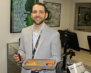 A.J. Caraballo, pharmacist and general manager of gLeaf Medical Cannabis on Youngstown Road, Warren, stands in front of a list of the types of medical marijuana dispensed in the sales area and holds a vaporizer that is sold there. The facility, the first Mahoning Valley medical marijuana dispensary, opened Friday morning. Before the opening, Caraballo showed reporters the sales and consultation areas and explained some of the regulations. 