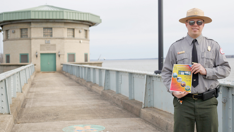 Bill Spring, resource manager at Mosquito Creek Lake, stands in front of the control tower at the lake while he holds a flier for the lake's 75th anniversary event taking place June 15. 