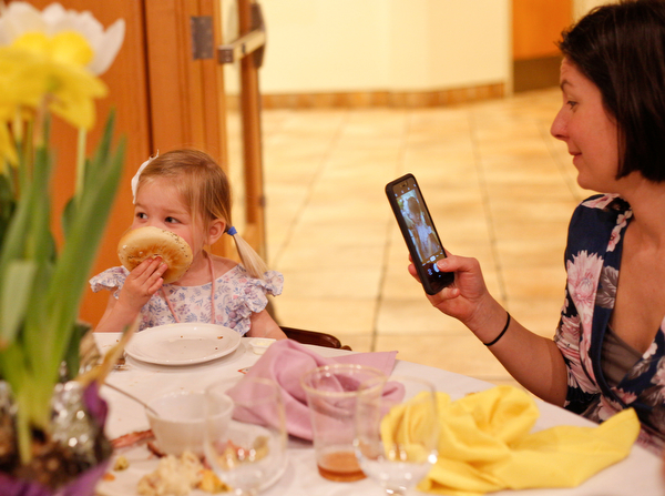 Beth Hawks, right, of Canfield, takes a photo of her daughter Claire Hawks, 2, as she eats a bagel at the annual Easter Brunch at Fellows Riverside Gardens on Sunday. EMILY MATTHEWS | THE VINDICATOR