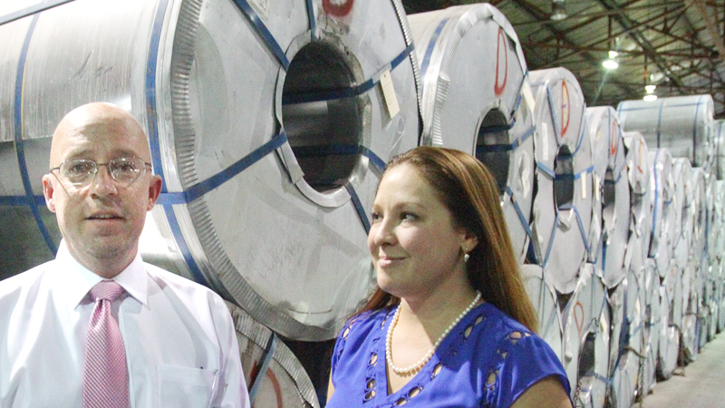 Specialty Strip and Oscillating Inc. President Adam VonPhilp and his wife and Vice President, Krissy VonPhilp, stand among coils of steel at the Masury plant that employs 30. Oscillating technology at the plant enables it to produce steel strips as long as 25 miles, significantly longer than those produced through conventional methods.