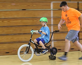 Seth Baker rides a specially adapted bike while Ryan Jones jogs to keep up at the iCAN Shine Bike Camp at Boardman Glenwood Junior High School. The camp continues through Friday.
