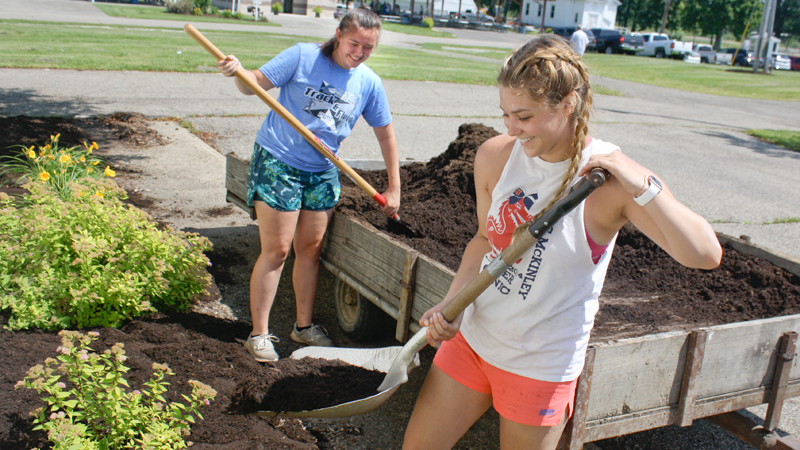 Alyssa Simmers of Howland, a student at Kent State University, right, works with Aleesha Tingler of Bristolville, spreading mulch at the Trumbull County Fairgrounds Thursday morning in preparation for the start of the fair Tuesday July 9. Both are workers for the fair board. Among the new attractions this year is drag racing.