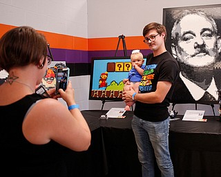 Abbey Stiles, left, takes a photo of her husband Steve Stiles and their 7-month-old daughter Freya, all of Austintown, in front of pieces made by members of NeoLUG, a group of adult hobbyists who share their passion for building with Legos, at the Youngstown Comic Con in Covelli Centre on Saturday afternoon. EMILY MATTHEWS | THE VINDICATOR