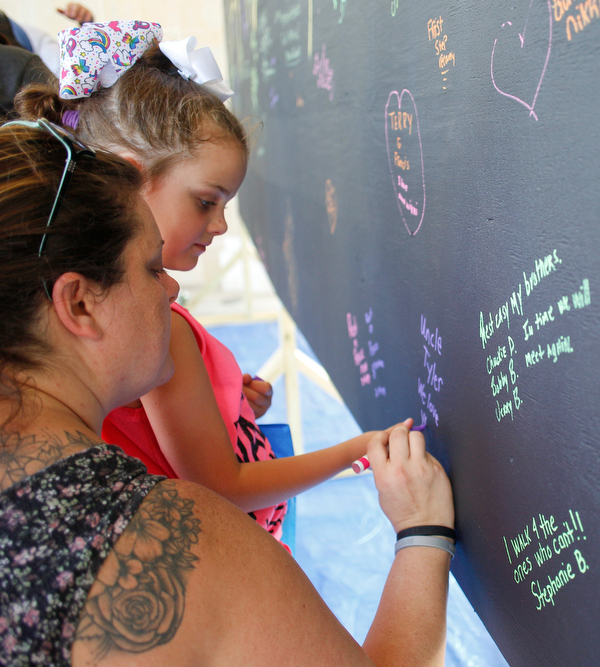 Amanda Humphreys, left, and her daughter Payge Humphreys, 6, both of Canfield, write a message for Amanda's brother-in-law Tyler, who passed away from a drug overdose, on a blackboard filled with written messages stating why people walk in the Warren Walk Against Heroin at the Warren Amphitheater on Sunday. EMILY MATTHEWS | THE VINDICATOR