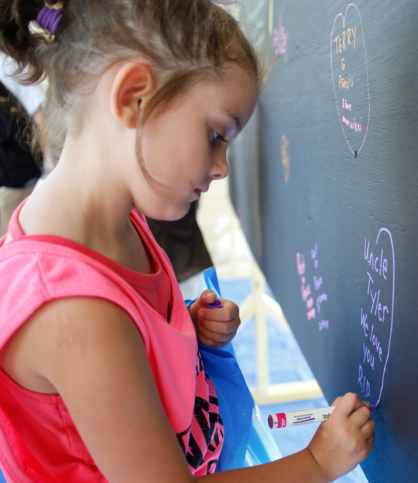 Payge Humphreys, 6, of Canfield, draws a heart around a message for her uncle Tyler, who passed away from a drug overdose, on a blackboard filled with written messages stating why people walk in the Warren Walk Against Heroin at the Warren Amphitheater on Sunday. EMILY MATTHEWS | THE VINDICATOR