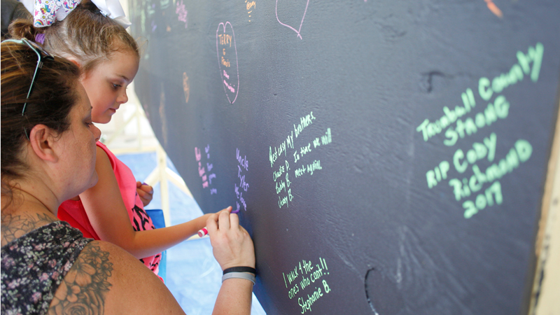 Amanda Humphreys, left, and her daughter, Payge Humphreys, 6, both of Canfield, write a message on a blackboard for Amanda’s brother-in-law, Tyler, who died from a drug overdose. The blackboard is filled with written messages stating why people walked in the Warren Walk Against Heroin at the Warren Community Amphitheatre on Sunday. 