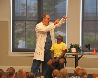 Neighbors | Jessica Harker .Dr. Cletus Beaker put sharp pencils through a plastic bag full of water over the head of a volunteer on July 12 at the Canfield library's Hillbilly Silly Science Show.