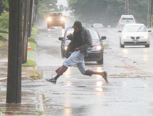 William D. Lewis the vindicator A pedestrian jumps across a puddle on East Market St in Warren Tuesday afternoon shortly after a fast moving storm hit the area downing trees and dumping heavy rain.