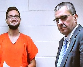 James Reardon, left, smiles as he is arraigned via video Monday in Struthers Municipal Court on charges he threatened to shoot up the Jewish Community Center in Youngstown. He was ordered held on 10 percent of $250,000 bond. To the right is Atty. Walter Ritchie, who represents clients who appear for arraignments via video hookup from the jail.