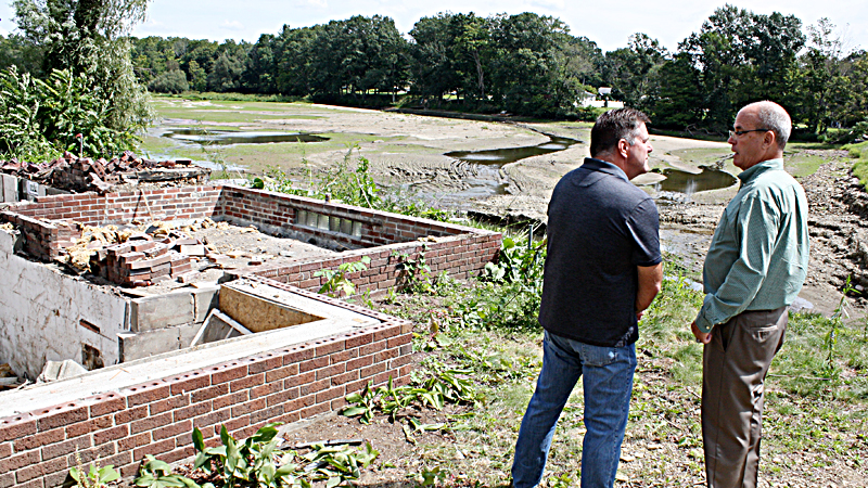 Randy Smith, Trumbull County engineer, left, and State Rep. Michael O’Brien of Warren, D-64th, stand near a home being demolished and the area where the Kinsman Lake causeway washed away, at far right, July 20. Also in the background is the former Kinsman Lake, which is now a stream. Smith, O’Brien and other officials were there Monday to announce the start of the $1.85 million in repairs to the causeway.
