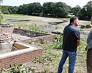 Randy Smith, Trumbull County engineer, left, and State Rep. Michael O’Brien of Warren, D-64th, stand near a home being demolished and the area where the Kinsman Lake causeway washed away, at far right, July 20. Also in the background is the former Kinsman Lake, which is now a stream. Smith, O’Brien and other officials were there Monday to announce the start of the $1.85 million in repairs to the causeway.
