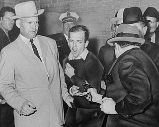 In this Nov. 24, 1963 file photo, Lee Harvey Oswald reacts as Dallas night club owner Jack Ruby, foreground, shoots at him from point blank range in a corridor of Dallas police headquarters. At left is Detective Jim Leavelle. The longtime Dallas lawman who was captured in one of history's most iconic photographs as he escorted President John F. Kennedy's assassin moments before he was fatally shot, died Thursday. He was 99.